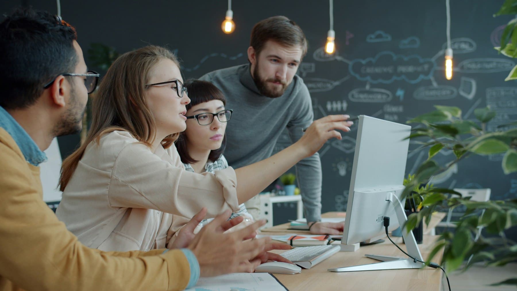 Four colleagues reviewing work together calmly around a desktop monitor